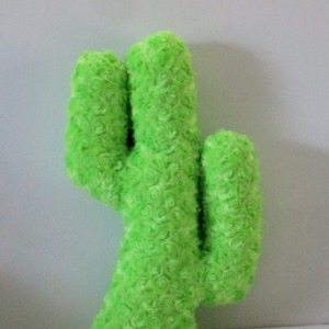 May include: A plush, lime green cactus-shaped pillow. The pillow has a textured, curly fabric and a three-dimensional design. The cactus has three upright sections and a short base.