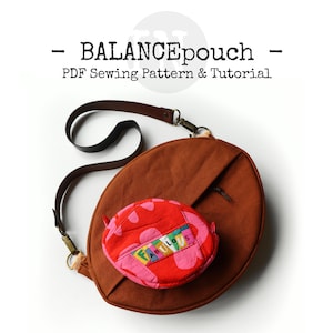 Könnte beinhalten: Eine braune runde Umhängetasche mit einem schwarzen Riemen und einer kleineren roten und pinkfarbenen Tasche mit dem Wort "FABULOUS" darauf. Die Tasche befindet sich auf einem weißen Hintergrund.  PDF-Nähmuster und Anleitung.
