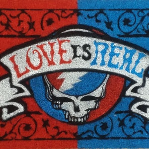 May include: A red and blue doormat with a black border and a white banner that says "LOVE IS REAL". The banner is wrapped around a blue and red skull with a lightning bolt.