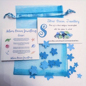 May include: A blue organza bag with a white card that reads "Silver Ocean Jewellery" and includes care instructions for the jewelry. The card is surrounded by small blue paper flowers.