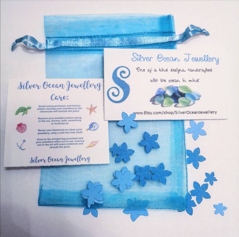 May include: A blue organza bag with a white card that reads "Silver Ocean Jewellery" and includes care instructions for the jewelry. The card is surrounded by small blue paper flowers.