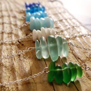May include: A set of necklaces with different colored sea glass beads. The necklaces are made with silver chains and feature various shades of blue, green, and white sea glass.