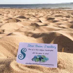 Pode incluir: Um cart&atilde;o de visita para Silver Ocean Jewellery, uma empresa que fabrica joias artesanais inspiradas no oceano. O cart&atilde;o apresenta um design de vidro do mar azul e verde e o texto "Designs &uacute;nicos, feitos &agrave; m&atilde;o com o oceano em mente." e "www.Etsy.com/shop/SilverOceanJewellery".