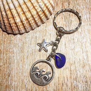 May include: A silver key chain with a charm of a wave design, a blue glass charm, and a silver star charm.