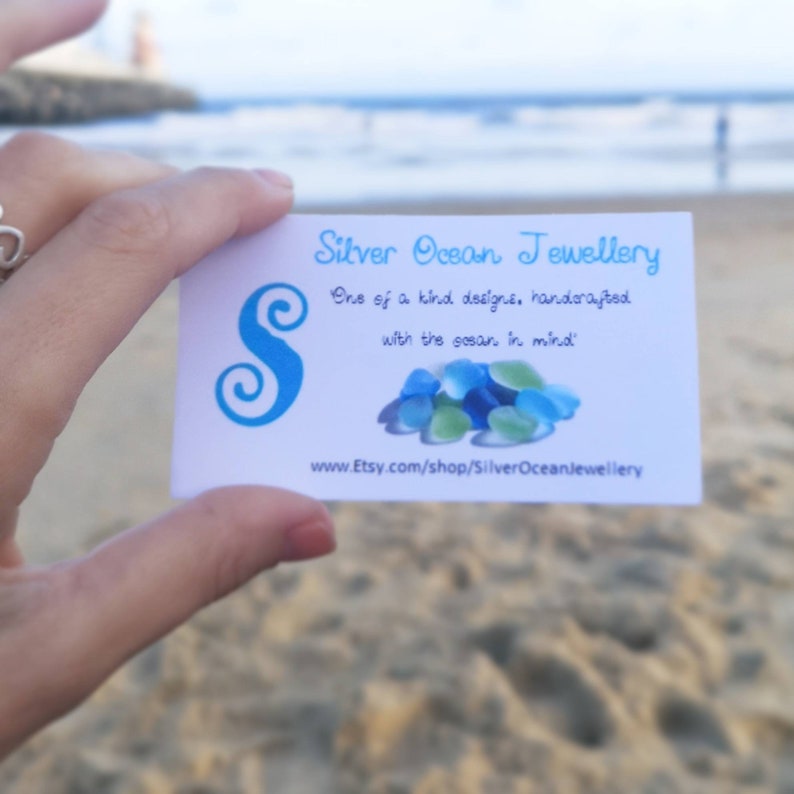 May include: A white business card with blue text and a blue swirl letter 'S' for Silver Ocean Jewellery. The text reads 'One of a kind designs, handcrafted with the ocean in mind'. The website address is www.Etsy.com/shop/SilverOceanJewellery.