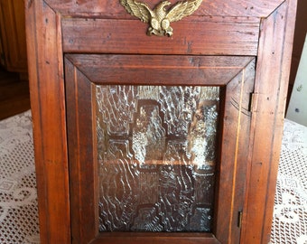 A Rustic Crusty Wood Wall Cabinet With A Plexiglass Frosted Decorative Front Window And A Metal Gold Eagle Decor With An Early American Look