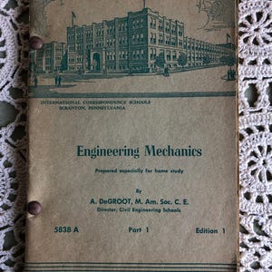 May include: Vintage book cover for "Engineering Mechanics" by A. DeGroot, Part 1, Edition 1. The cover is tan with green text and a detailed illustration of a building. The book is from the International Correspondence Schools, Scranton, Pennsylvania.