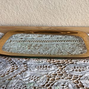 May include: A gold-rimmed glass serving tray with a clear glass center. The tray is sitting on a white lace tablecloth.