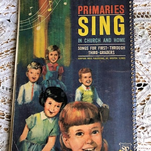 May include: Vintage spiral-bound book titled "Primaries Sing" with illustrations of children. The cover features the text in yellow and white, with a blue background and colorful vertical stripes. The book is for first- through third-graders.