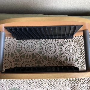 May include: A wooden CD rack with a light brown finish and two black plastic storage compartments. The rack is supported by two silver metal legs. The rack is designed to hold CDs and keep them organized.