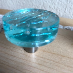 May include: A light blue glass cabinet knob with a swirl pattern. The knob is attached to a silver metal base.