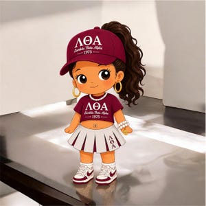 May include: A cartoon character wearing a maroon baseball cap with the text Lambda Theta Alpha 1975, a matching maroon crop top with the same text, a white pleated skirt with the Greek letters LTA, gold hoop earrings, and white sneakers.