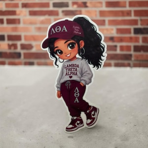 May include: A die-cut sticker featuring a cartoon character wearing a maroon baseball cap with the Greek letters ΛΘΑ, a light gray sweatshirt with the text LAMBDA THETA ALPHA, maroon sweatpants with the letters ΛΘΑ, and maroon and white sneakers.