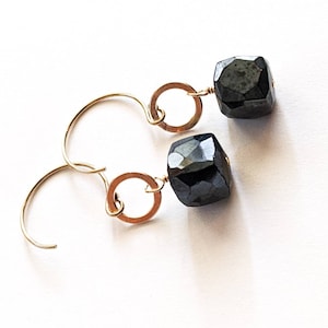 May include: A pair of gold hoop earrings with black faceted gemstone drops. The earrings are simple and elegant.