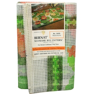May include: A white, green, and orange rug hooking pattern with a floral design. The pattern is labeled "Bernat No-Frame Rug Pattern No. 3405 Nasturtiums".