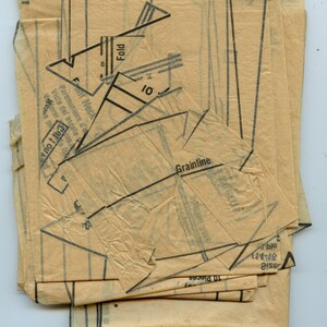 May include: A stack of vintage sewing pattern pieces in beige paper with black printed lines and text. The text includes "Fold", "Front Neck", "Grainline", and "10 Pieces".