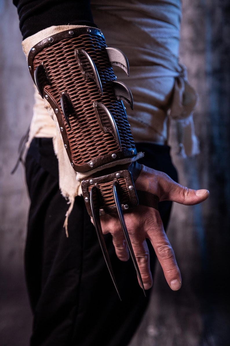 May include: A brown leather wrist cuff with metal spikes. The cuff is worn on the left wrist of a person.