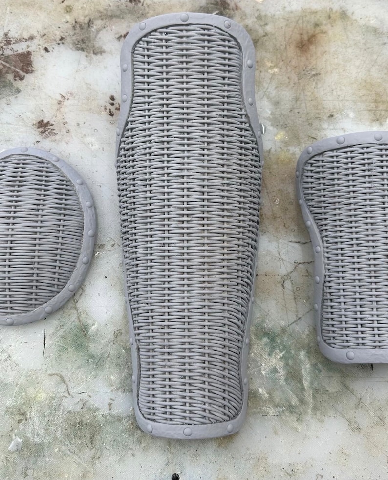 May include: Three gray, woven, protective pads with metal accents. The pads are shaped like a leg, a knee, and a shin.