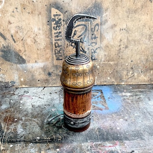 Puede incluir: Un tapón de botella decorativo de metal con acabado dorado y marrón. El tapón presenta una parte superior en forma de gancho y detalles intrincados.