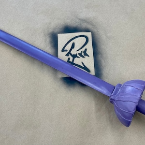 Puede incluir: Una espada de plástico púrpura con una empuñadura redondeada. La espada está sobre una superficie marrón.