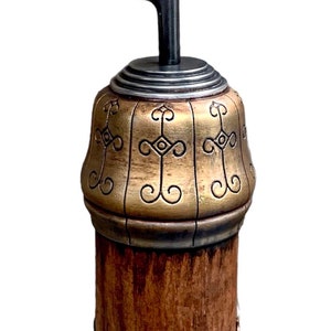 Puede incluir: Un gancho decorativo con un acabado dorado y marrón. El gancho está hecho de metal y tiene una base de madera. El gancho tiene forma de media luna y tiene un diseño decorativo en la base.
