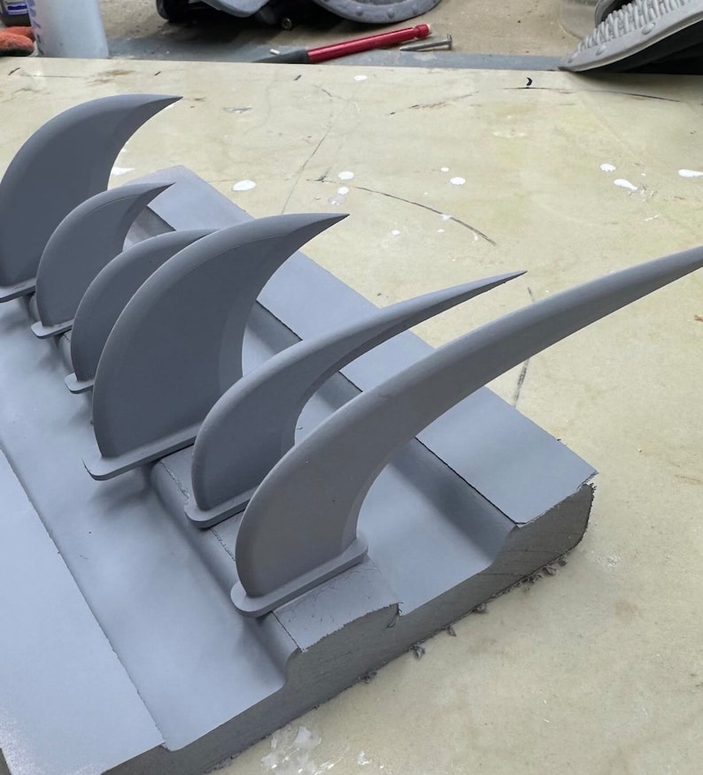 May include: A set of five gray plastic fin-shaped objects are attached to a gray foam base. The fins are arranged in a row, with the largest fin at the back and the smallest fin at the front.