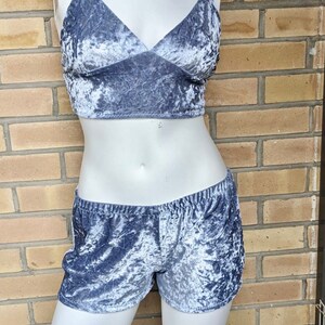 May include: A two-piece set of gray crushed velvet pajamas. The top is a cropped tank top with thin black straps and a V-neck. The shorts are high-waisted and have a wide elastic waistband.