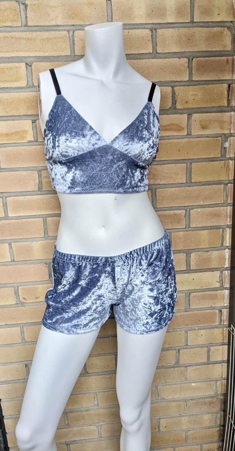 May include: A two-piece set of gray crushed velvet pajamas. The top is a cropped tank top with thin black straps and a V-neck. The shorts are high-waisted and have a wide elastic waistband.