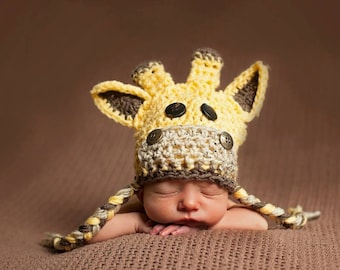 May include: A baby wearing a crocheted giraffe hat with brown and yellow yarn. The hat has brown buttons for eyes and a brown nose.
