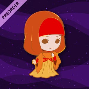 May include: A cartoon enamel pin featuring a character in orange and yellow robes with a red head covering. The pin has a purple background with white stars and the word "PREORDER" in a diagonal banner.