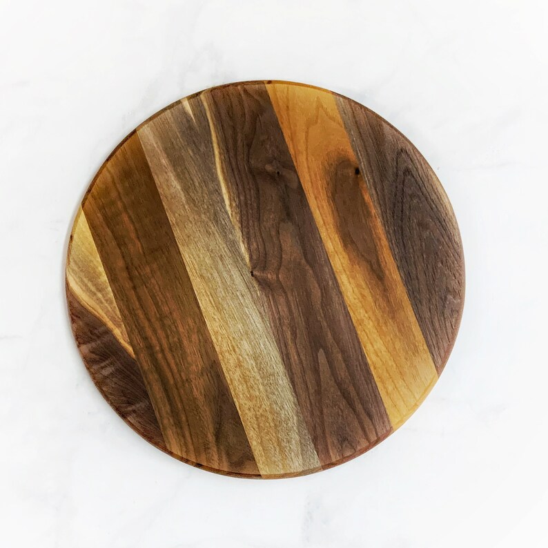 May include: A round wooden serving tray with a natural wood finish. The tray is made of multiple pieces of wood that are joined together to create a striped pattern.