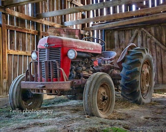 May include: A red vintage tractor with a rusty metal grill and a large rear tire, parked inside a wooden barn.