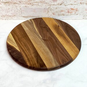 May include: A round wooden serving board with a striped pattern. The board is made of walnut wood and has a natural finish.