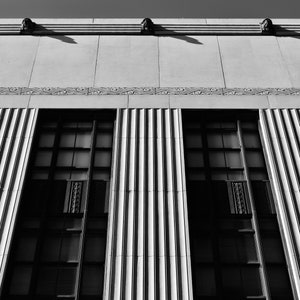 May include: Black and white photo of a building with three large windows and a decorative cornice. The windows are divided into multiple panes and are framed by vertical columns.