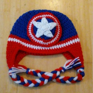 May include: A blue, red, and white crocheted hat with a white star on a red, white, and blue circle. The hat has a long braided cord.