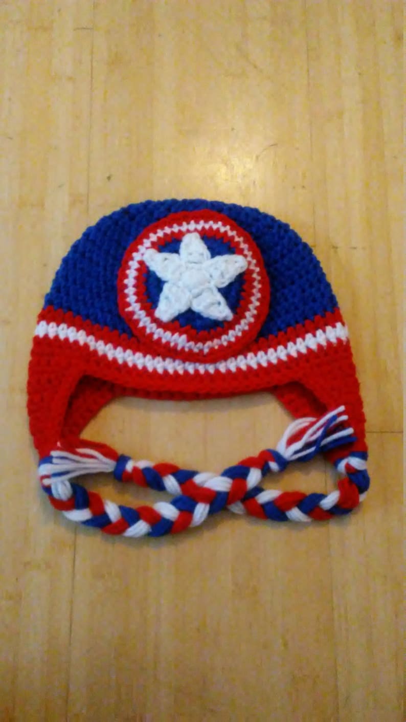 May include: A blue, red, and white crocheted hat with a white star on a red, white, and blue circle. The hat has a long braided cord.