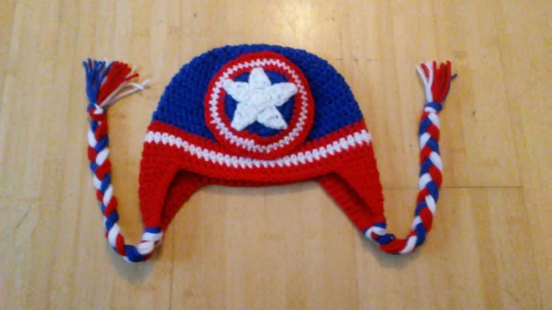 May include: A red, white, and blue crocheted hat with a star on the front. The hat has long ties that are braided.