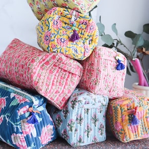 May include: A stack of six colourful quilted fabric pouches with floral patterns. The pouches have zipper closures and tassel pulls.