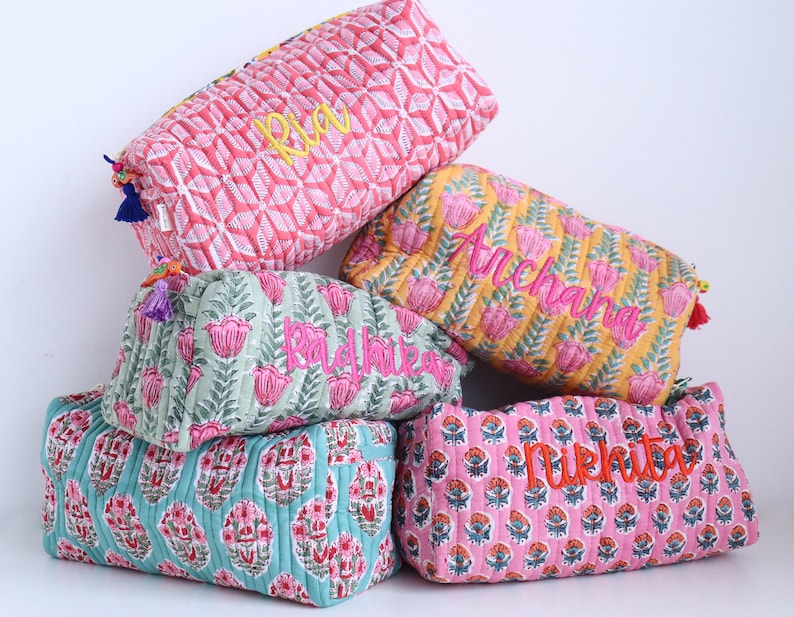 May include: A stack of five colorful quilted fabric pouches with embroidered names: Ria, Anchal, Radhika, Nikhita. The pouches are made of cotton and have a floral print.