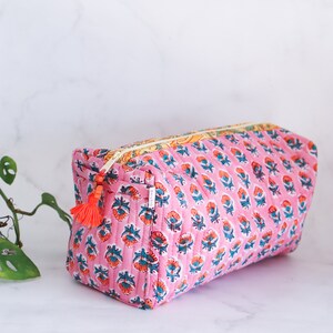 May include: Pink quilted makeup bag with a floral print and a tassel zipper pull.