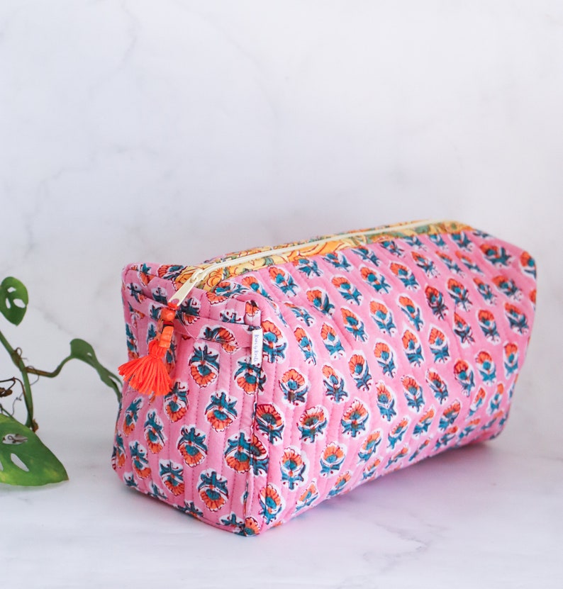 May include: Pink quilted makeup bag with a floral print and a tassel zipper pull.