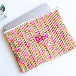 Puede incluir: Una funda para portátil amarilla con un estampado floral rosa y el nombre "Roni" bordado.