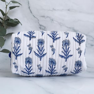 May include: White quilted makeup bag with a blue floral print. The bag has a zipper closure and a blue trim.