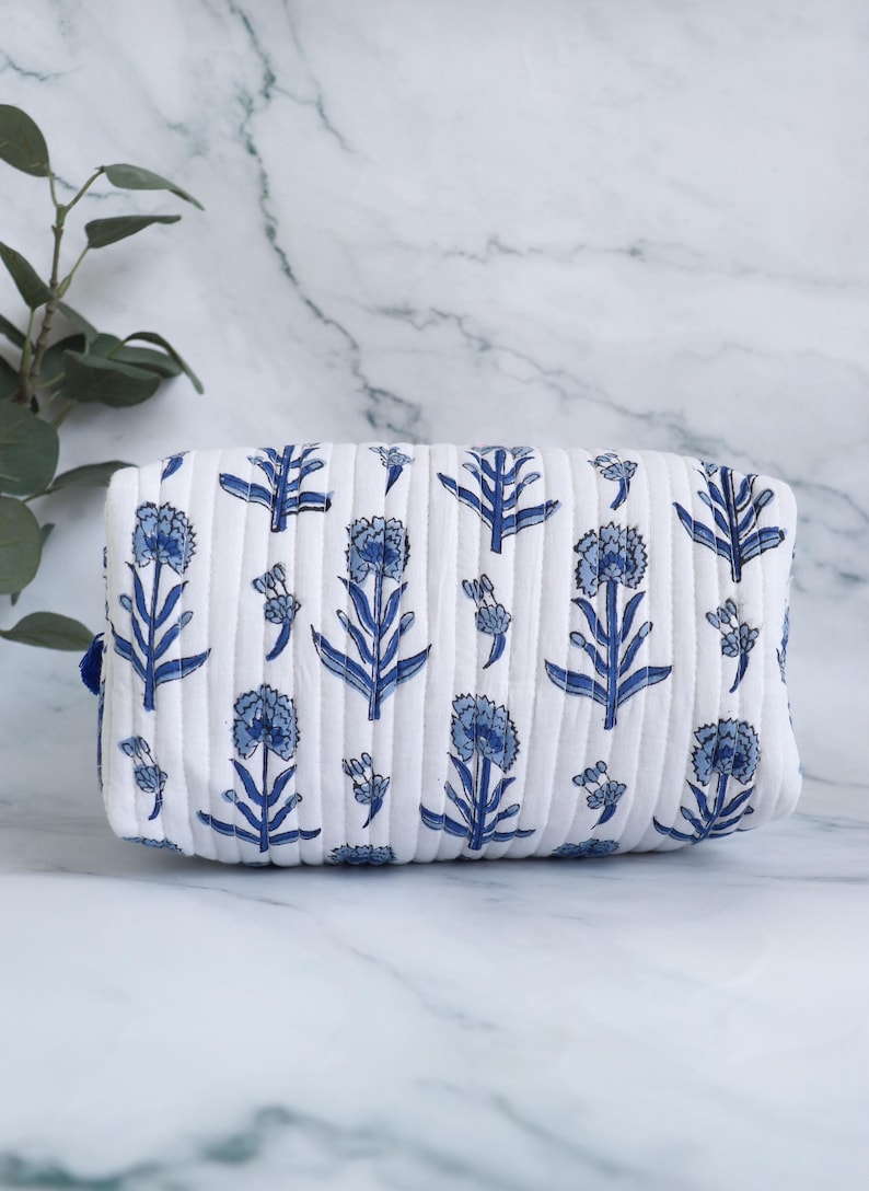 May include: White quilted makeup bag with a blue floral print. The bag has a zipper closure and a blue trim.