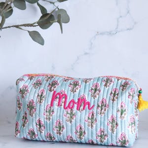 May include: A light blue quilted makeup bag with a floral print and the word "Mom" embroidered in pink.