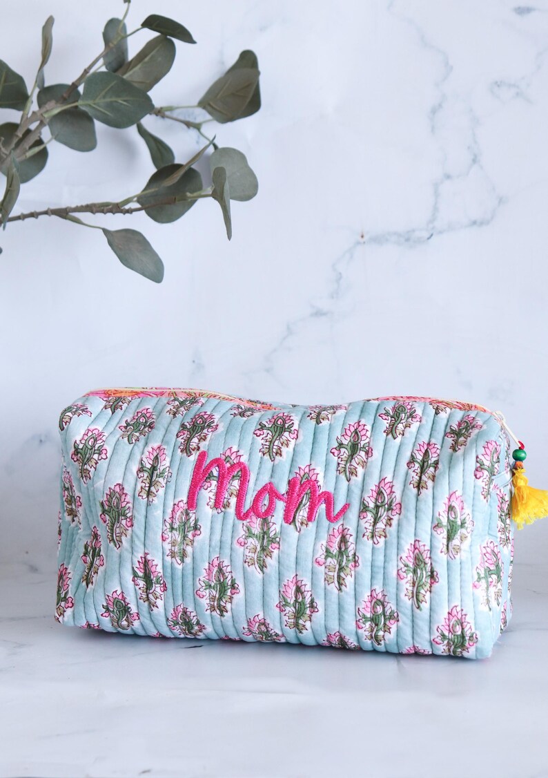 May include: A light blue quilted makeup bag with a floral print and the word "Mom" embroidered in pink.