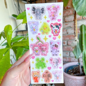 May include: A sheet of colorful stickers featuring cartoon animals. The stickers are on a white background with pink hearts and gold stars. The animals include a pig, cow, frog, chick, panda, and a red panda.