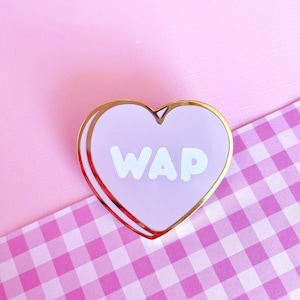 May include: A purple heart-shaped pin with a gold outline and the word "WAP" in white letters.