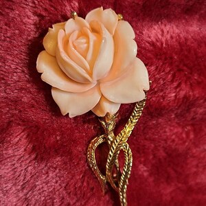 Può includere: Spilla a forma di rosa color pesca con stelo e foglie dorate. La rosa è il punto focale, con petali dettagliati. La spilla ha un design classico, adatta per aggiungere un tocco di eleganza a qualsiasi outfit.