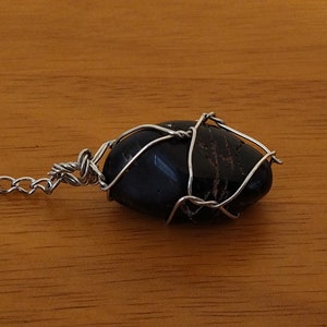 May include: A black stone pendant with silver wire wrapping, attached to a silver chain.